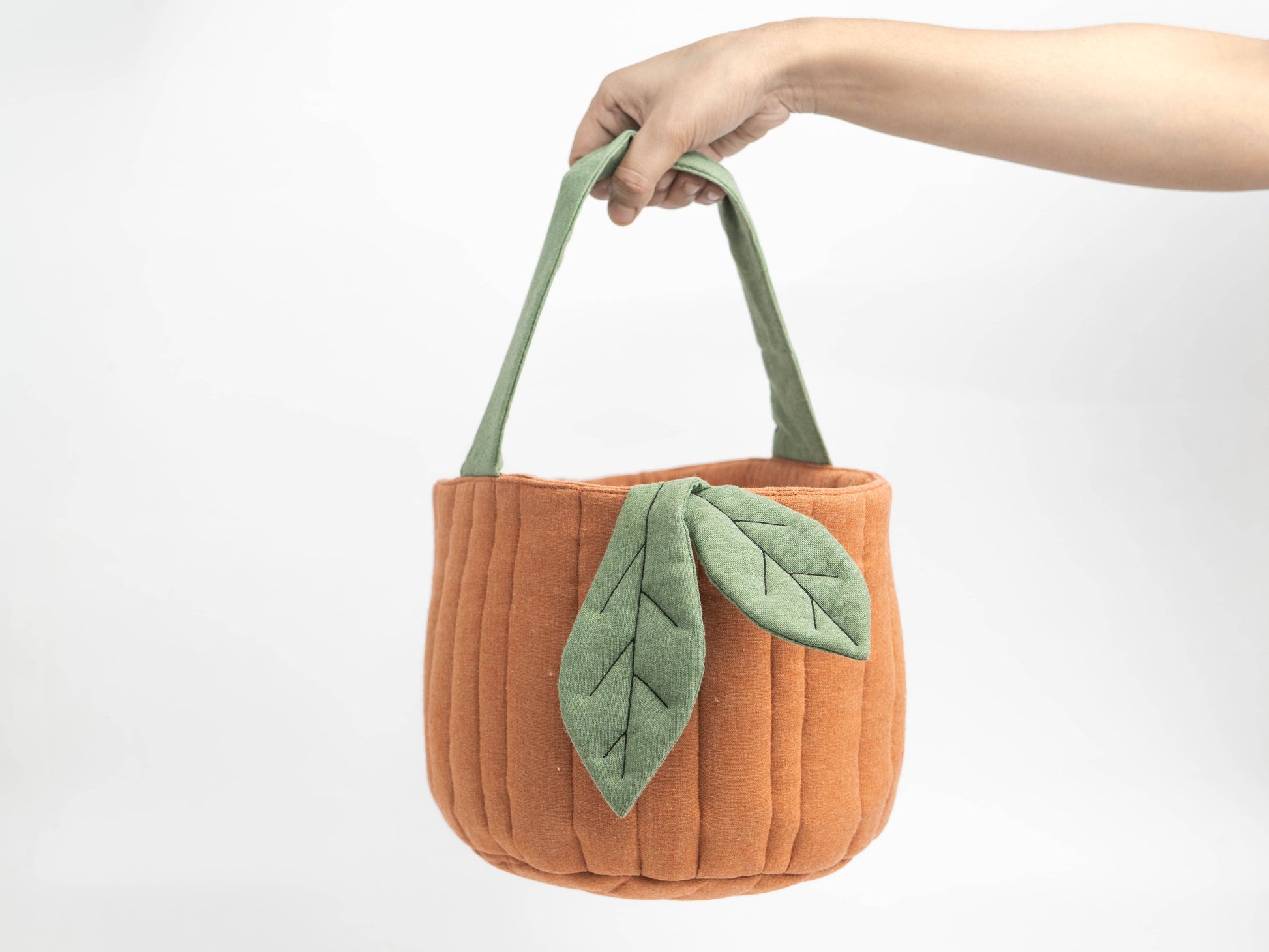 An orange felt tote bag with green fabric handles and a green leaf applique, held by a person's hand against a plain white background.