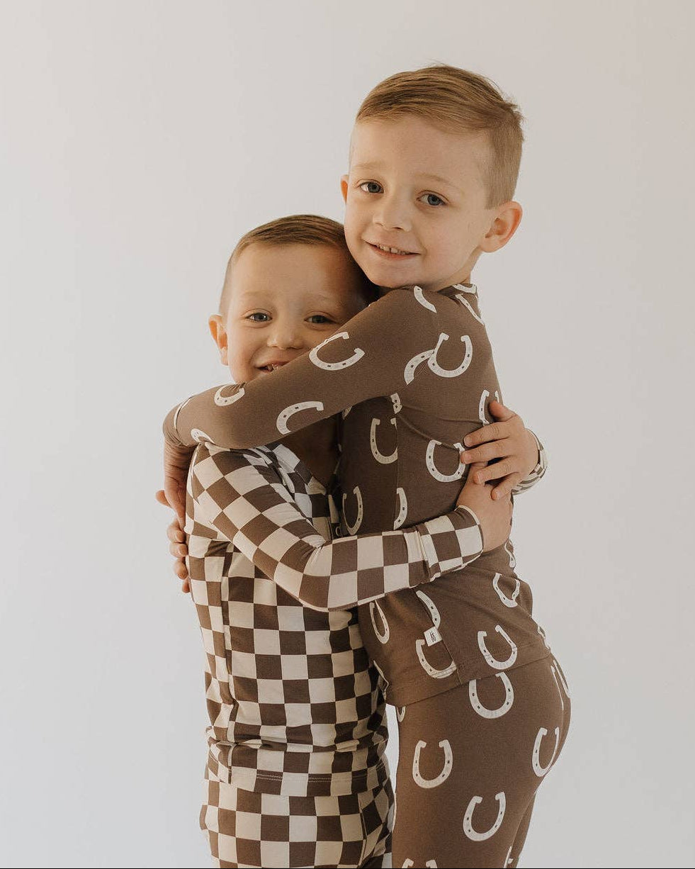 Two children wearing brown outfits with patterns, hugging each other against a white background.