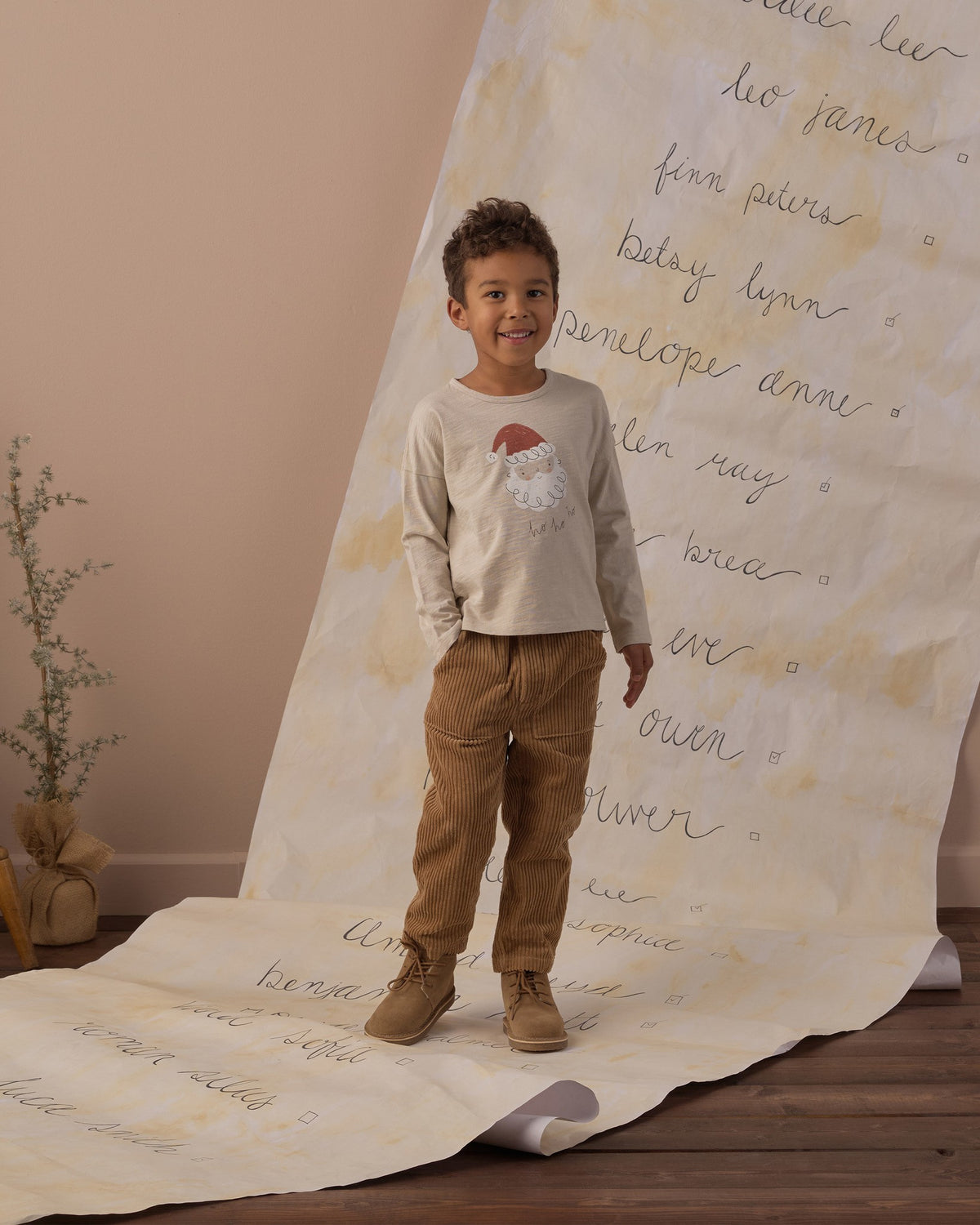 Boy standing on a handwritten backdrop wearing the Rylee + Cru Santa long sleeve tee and tan pants