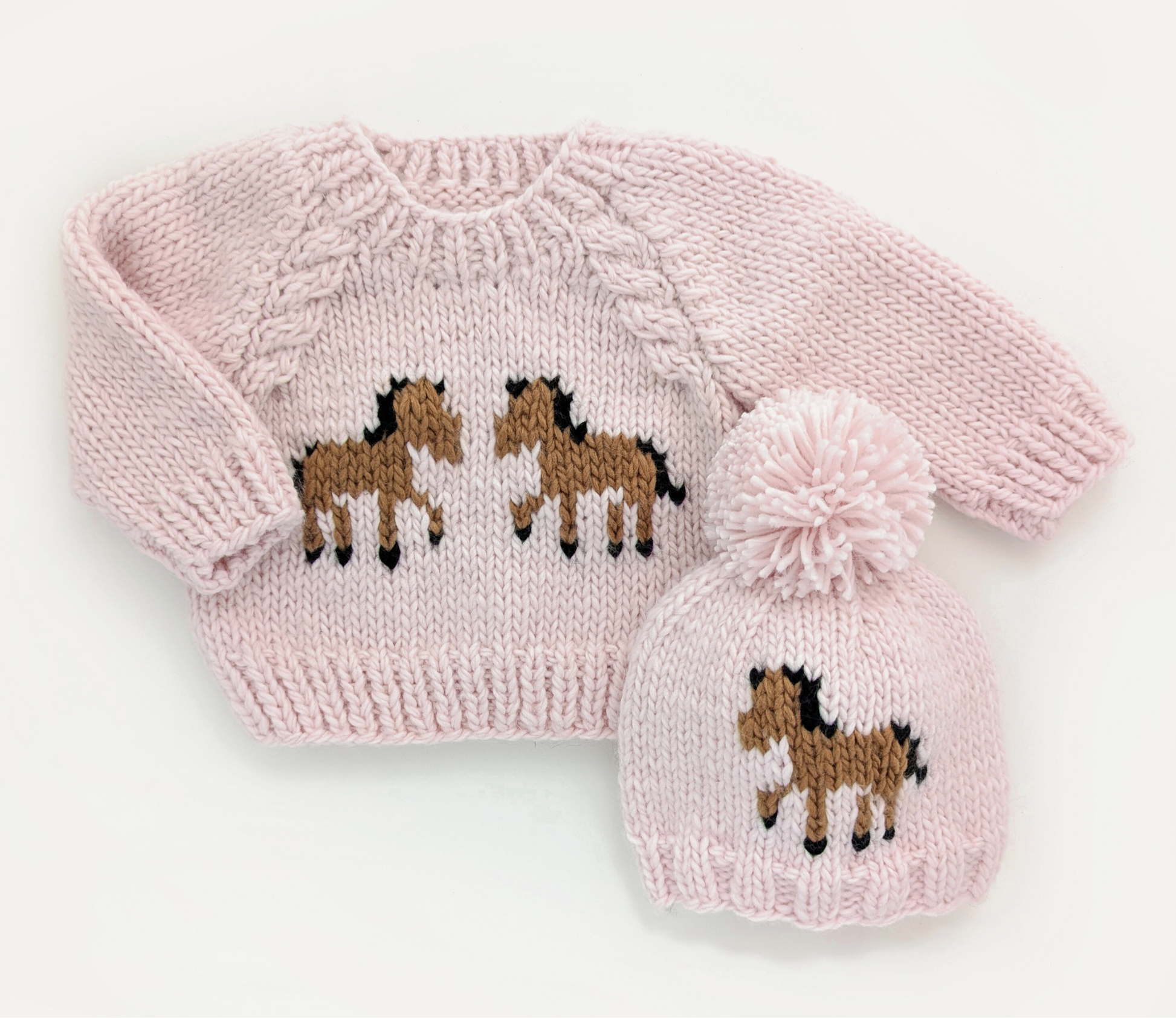 Pink knitted sweater and hat set with horse designs on a white background