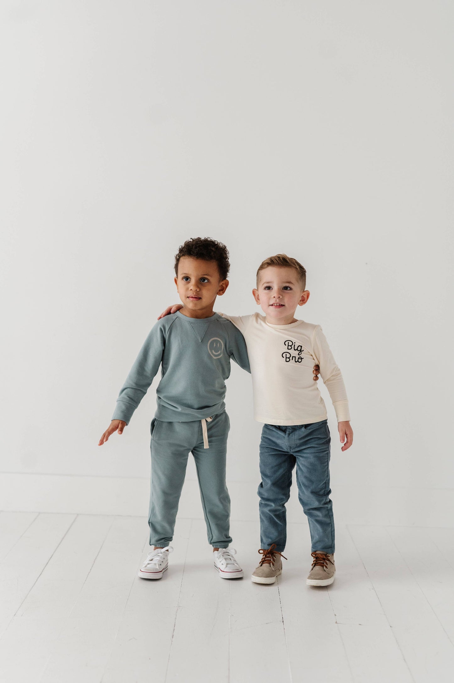 Two boys smiling. Boy on left is wearing our Smile Raglan Sweatshirt and boy on right is wearing our Big Bro longsleeve bamboo tee. 