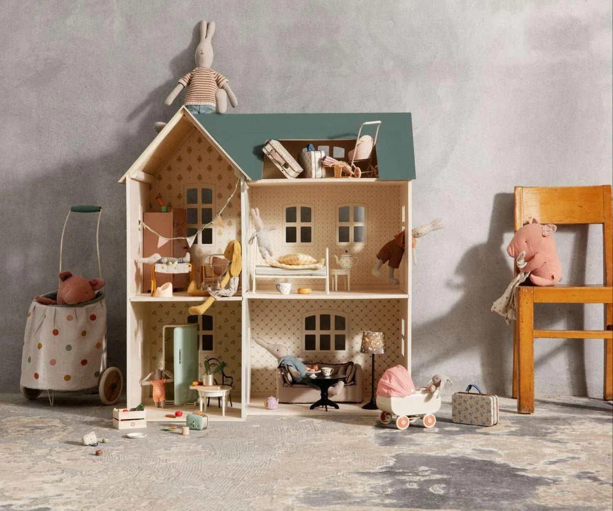 Dollhouse with furniture and toys on a textured floor against a gray wall