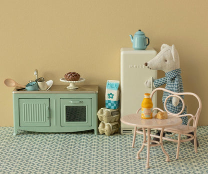 Miniature kitchen setup with a refrigerator, table, and various items on a patterned floor.