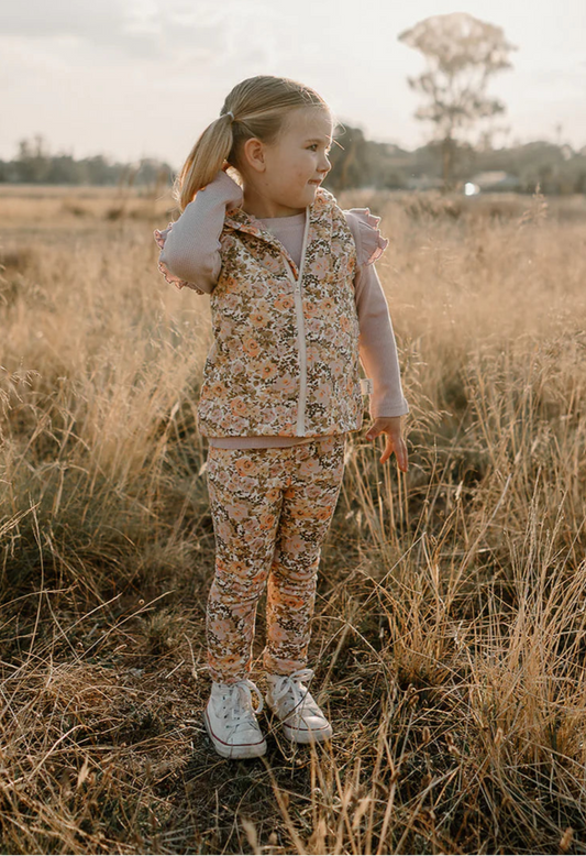 Girl smiling in a field while wearing her Florence Hooded Vest and Florence Fleece Leggings. 