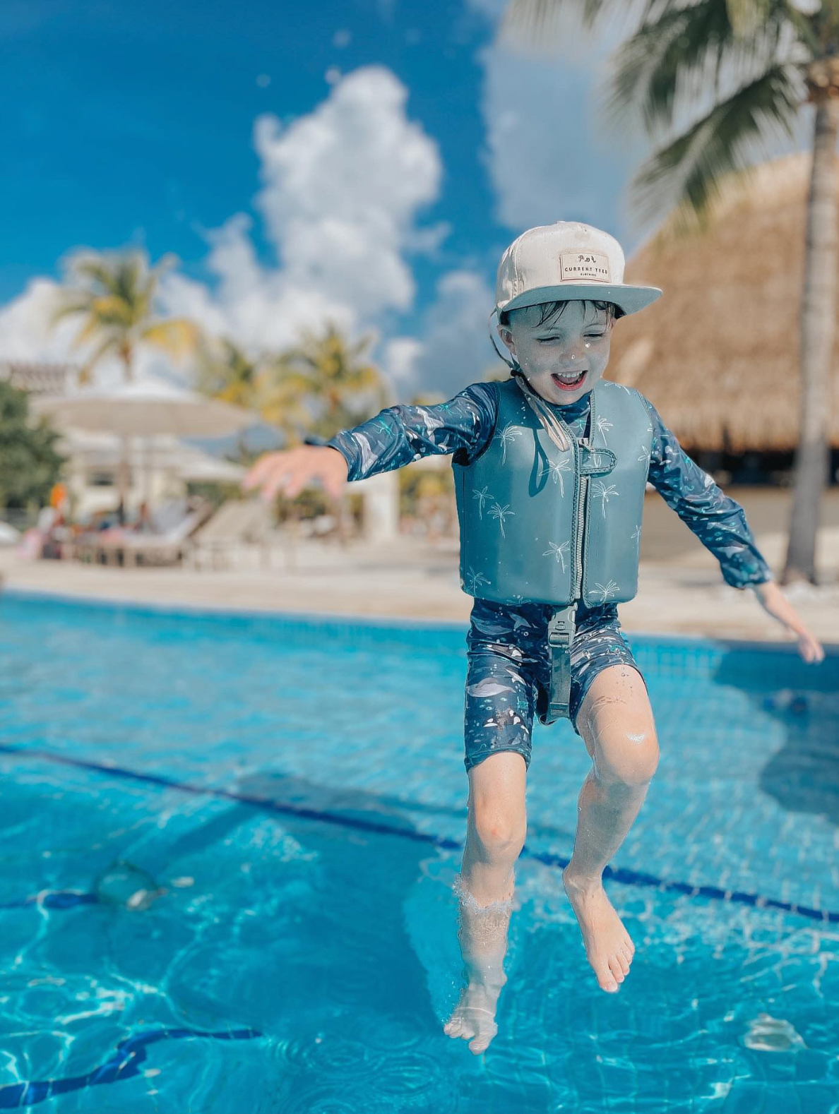 Boy jumping into pool wearing Green palm swim vest