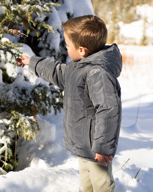 Boy reaching for a snowy branch in the reversible puffer worn with the solid midnight side out