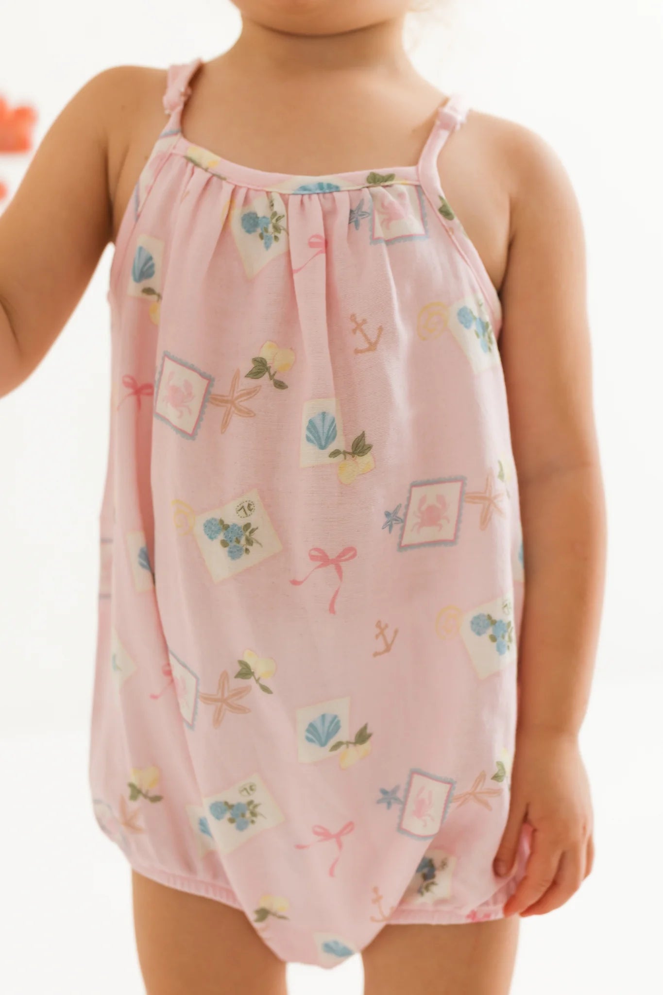 Child wearing a pink bubble romper with floral patterns on a white background