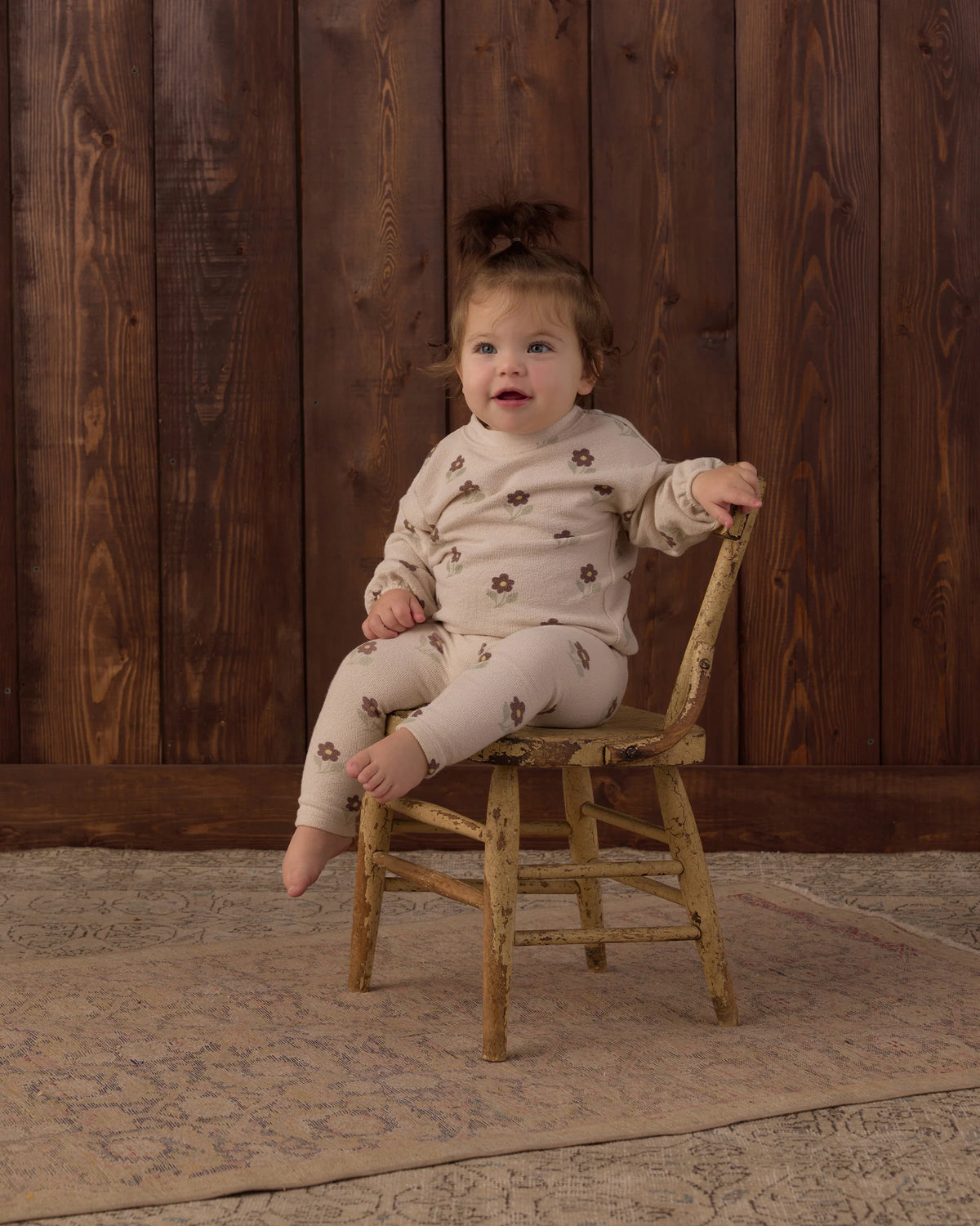 Toddler girl reaching out from a wooden chair in the blush Petal Daisy spongey knit set