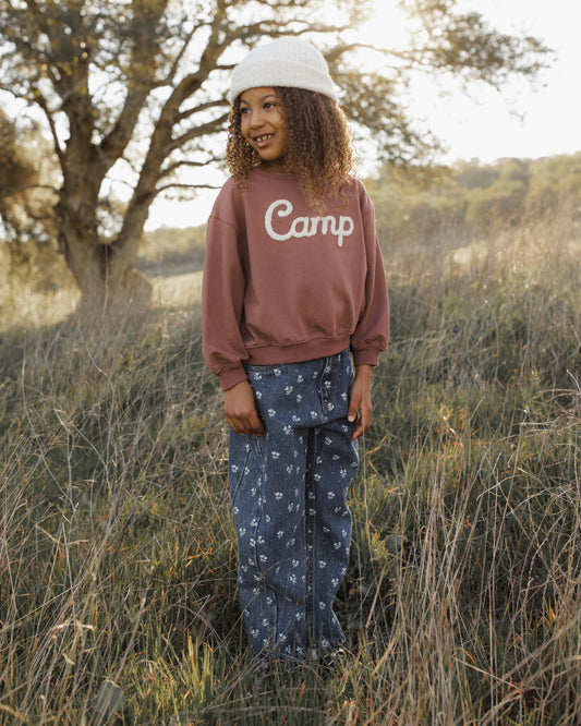 Child in a grassy field wearing Rylee + Cru Barrel Pants in Heart Ditsy indigo denim with a dusty rose Camp sweatshirt and white cap