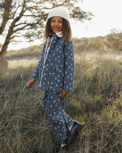A young child wearing a blue patterned long-sleeve top and matching pants with a white beanie, standing outdoors in a grassy field.