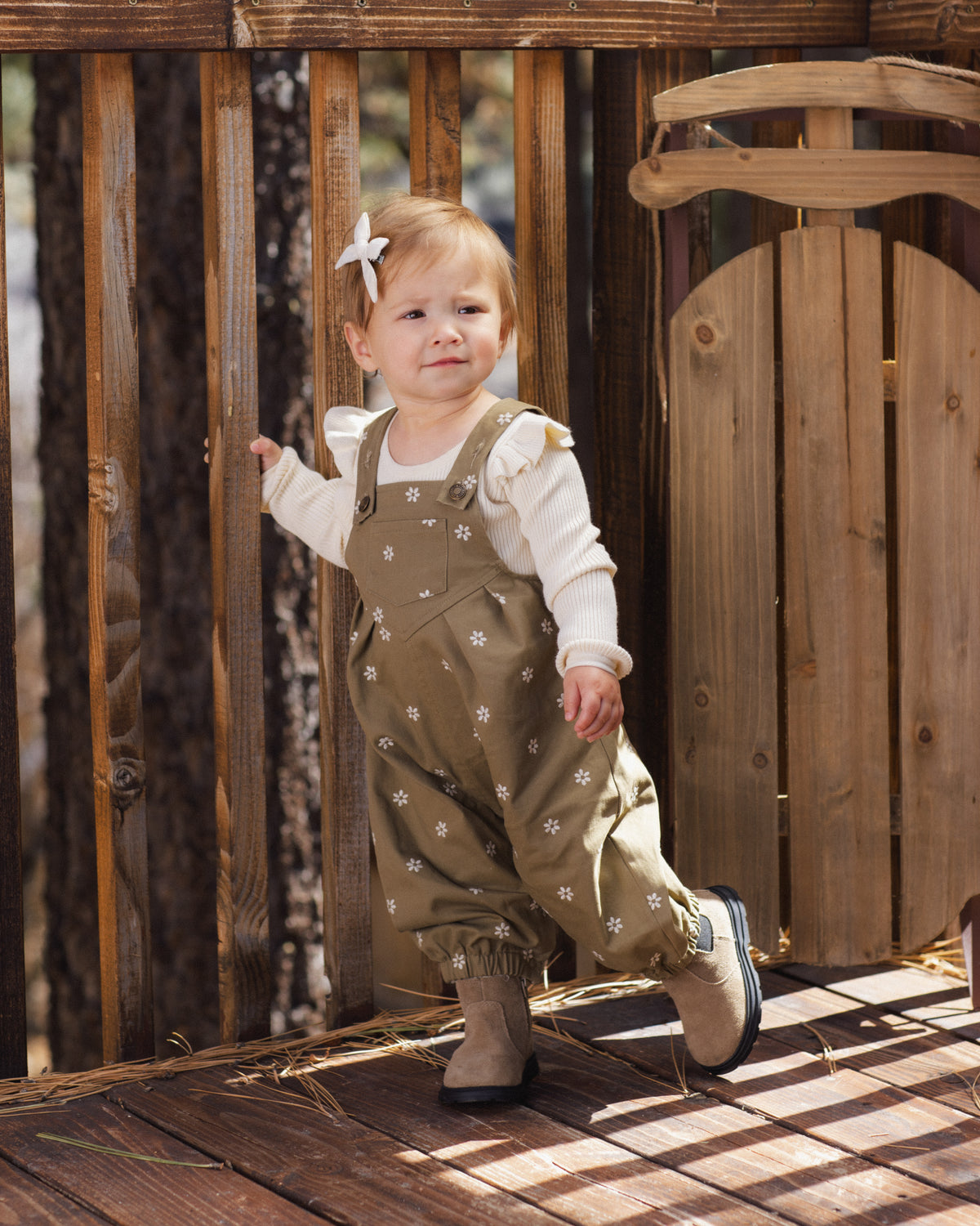 Toddler walking through a wooden gate in the olive embroidered daisy Vintage Overall