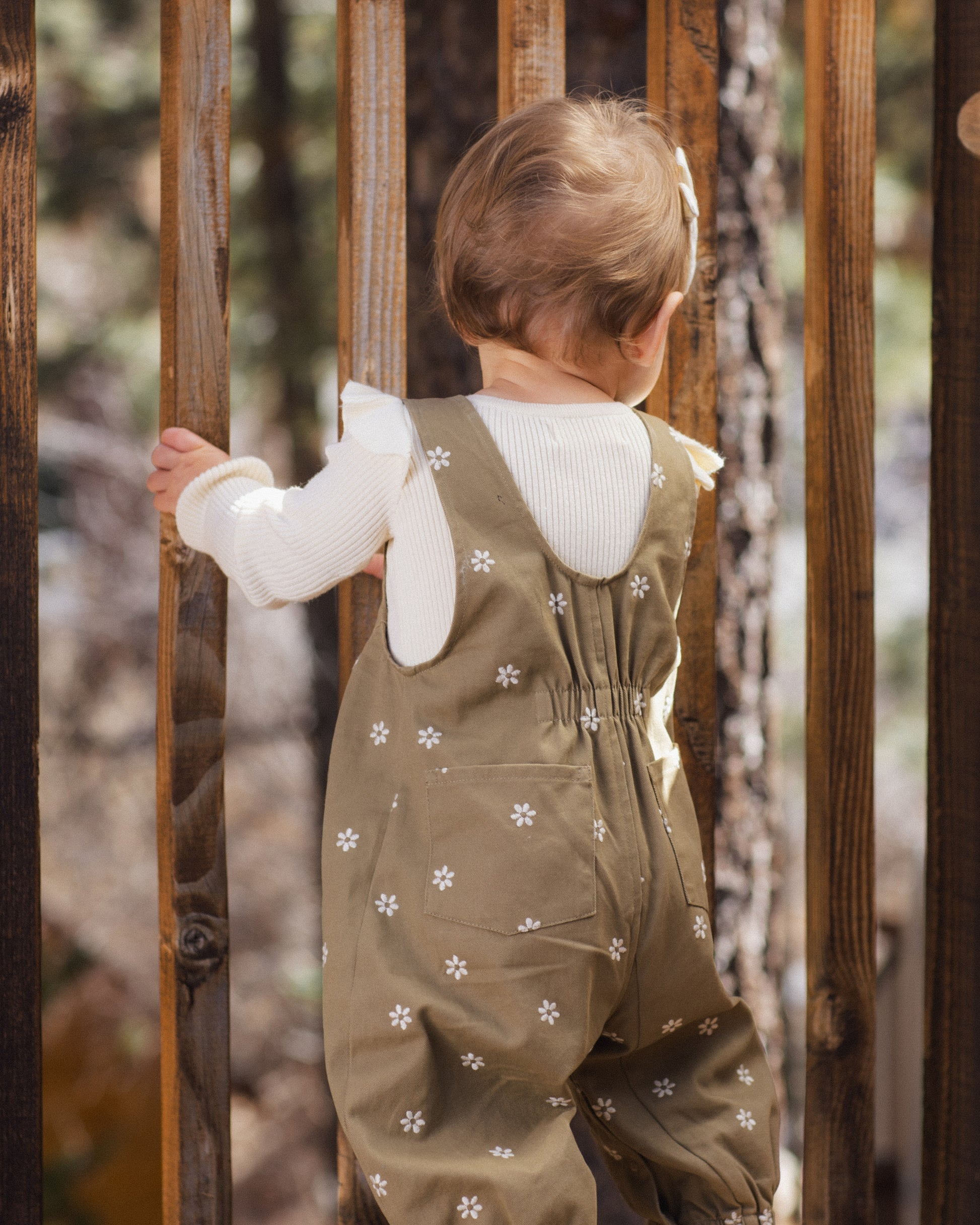 Toddler seen from behind in the Rylee + Cru Vintage Overall in olive with embroidered daisies