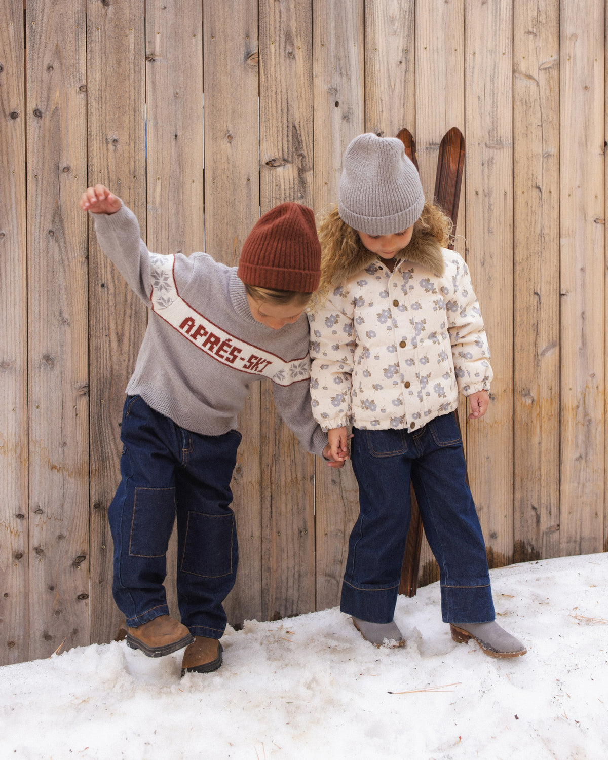 Two children playing in the snow by a wooden fence, one in the Reagan Apres Ski sweater