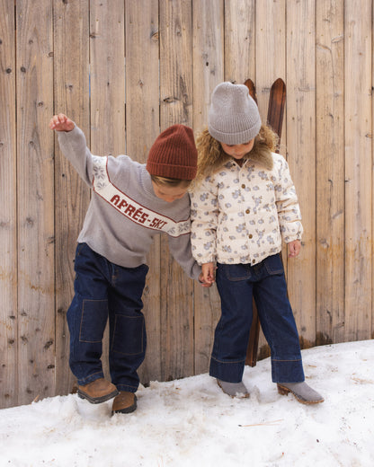 Two children playing in the snow by a wooden fence, one in the Reagan Apres Ski sweater