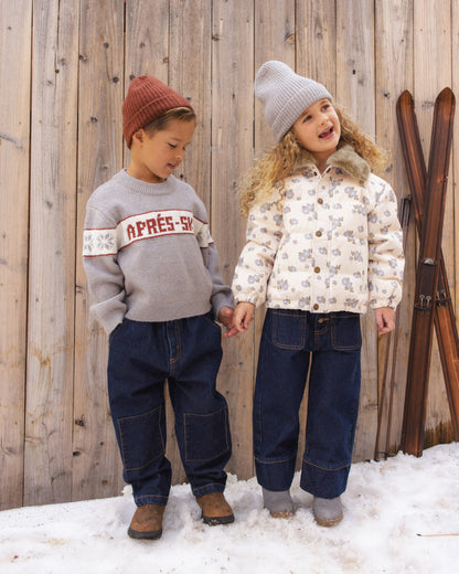 Two children standing in the snow, one wearing the Reagan Apres Ski sweater and rust beanie
