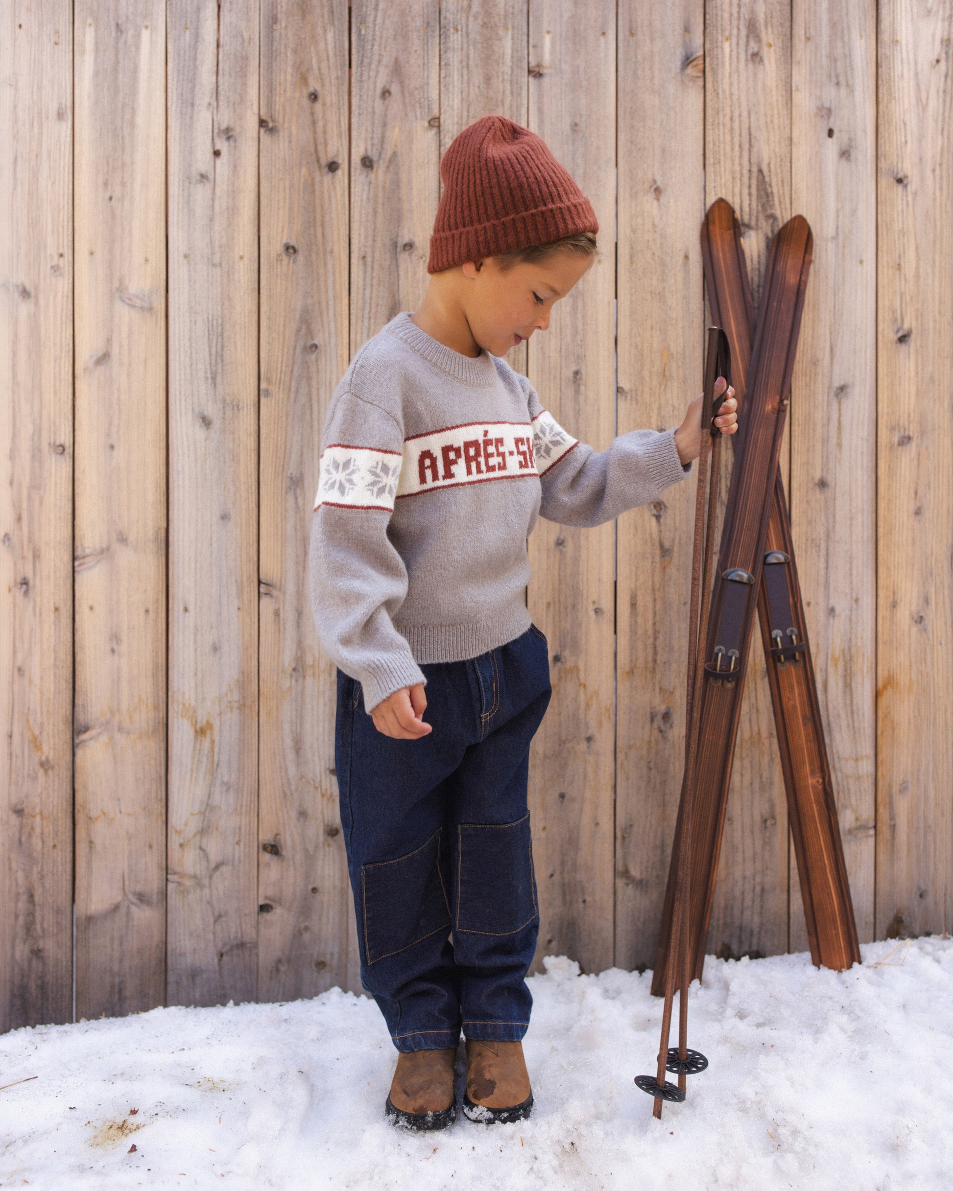 Child looking down beside wooden skis in the snow, wearing the Rylee + Cru Reagan Apres Ski sweater