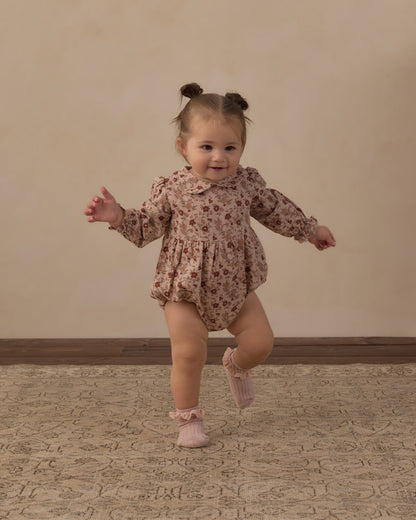 Toddler mid-step on a patterned rug in the Rylee + Cru Cora Romper in pink floral, with pink booties
