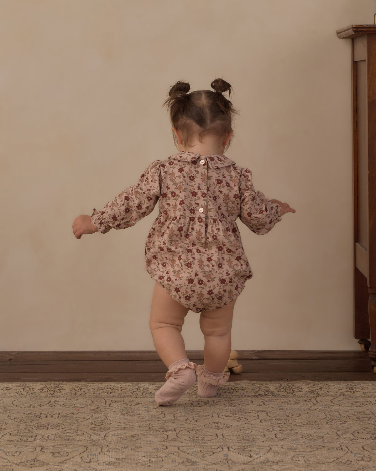 Toddler seen from behind in the Rylee + Cru Cora Romper in pink floral with pink ballet shoes