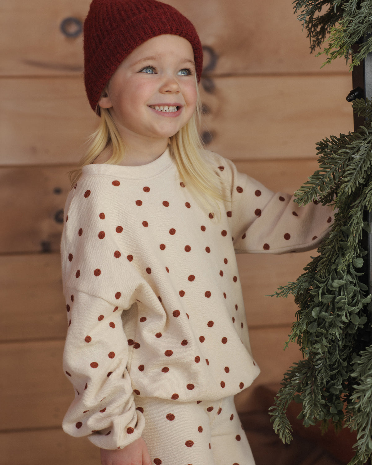 Girl smiling up at holiday greenery in the Rylee + Cru ruby dots spongey knit top