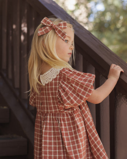 Back view of a girl with a hair bow wearing the Rylee + Cru Heidi dress in vintage plaid on a staircase