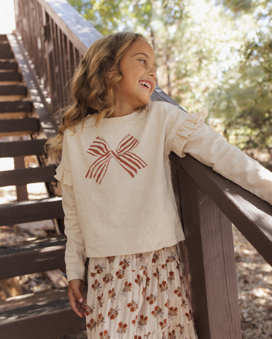 Girl on a wooden staircase outdoors wearing the Rylee + Cru ruffle long sleeve tee with a red striped bow graphic