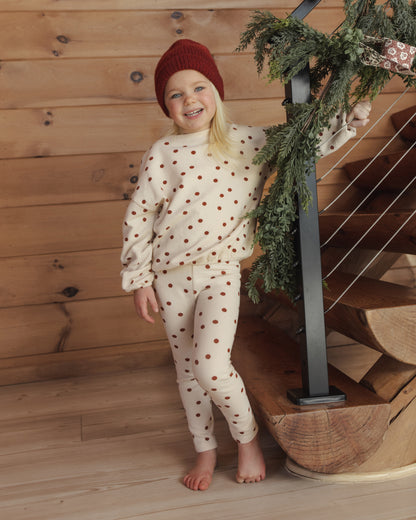 Girl in a red beanie wearing the Rylee + Cru spongey knit set in ruby dots on a wooden staircase with greenery