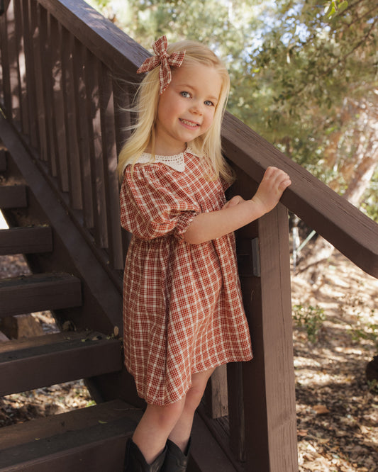 Girl on a wooden staircase outdoors wearing the Rylee + Cru Heidi dress in vintage plaid with a lace collar