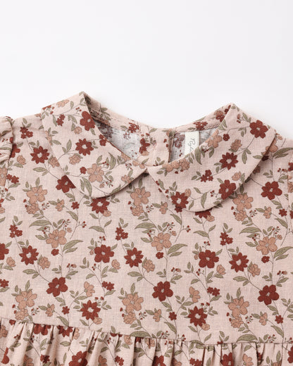 Close-up of a children's romper with a ruffled Peter Pan collar and a dusty floral print on a light beige linen-like fabric, featuring red and brown flowers with green leaves.