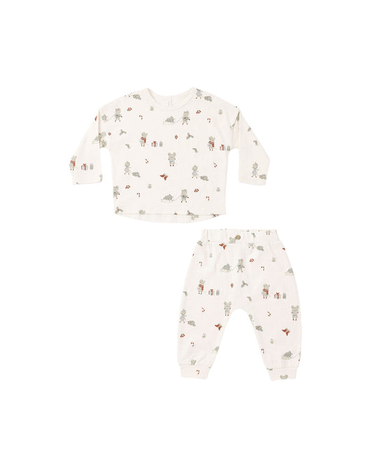 A two-piece baby pajama set featuring a long-sleeve top and matching pants in an off-white cotton fabric with a whimsical woodland animal print, laid flat on a white background.