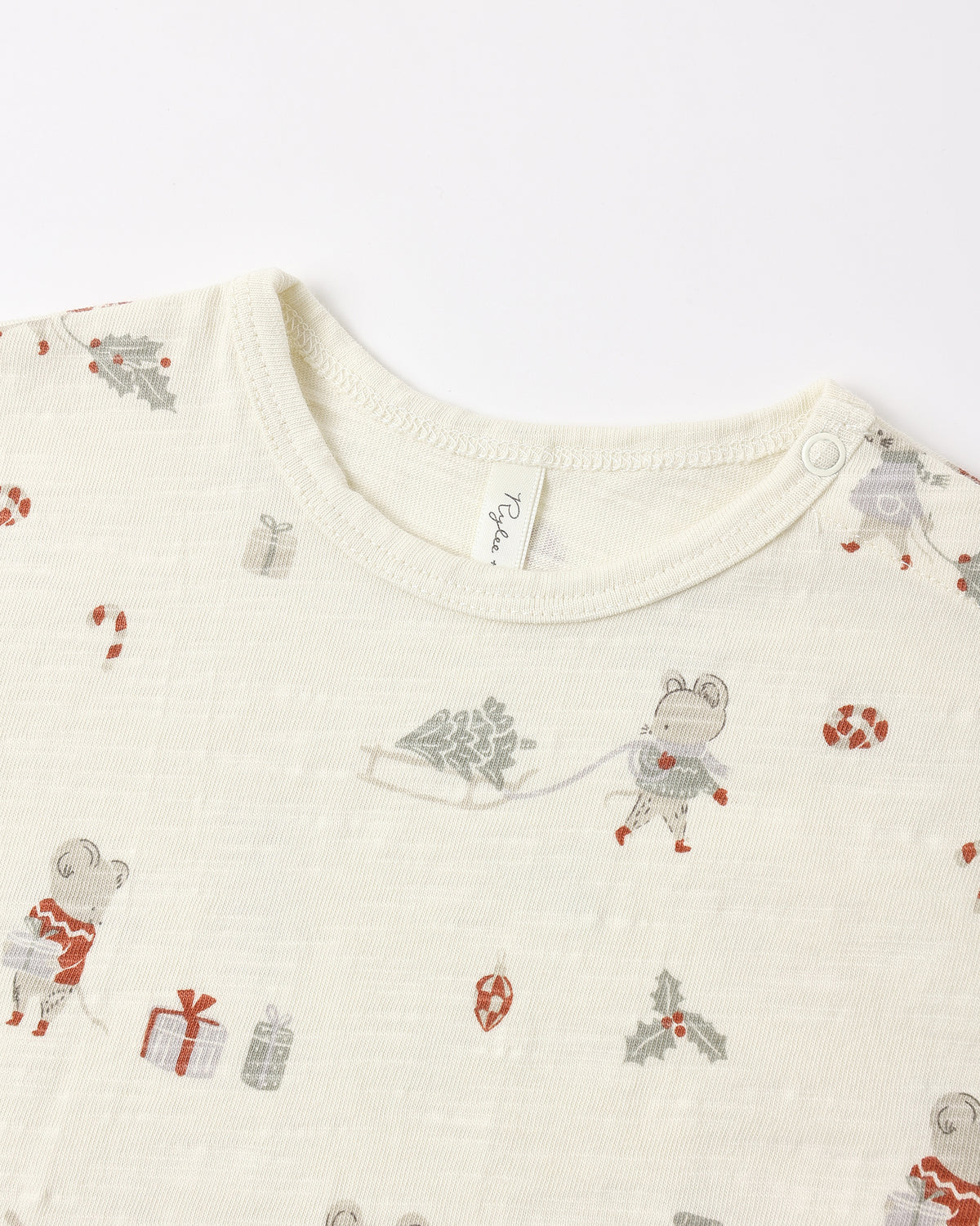 Close-up of a baby long-sleeve top in cream-colored cotton muslin fabric, featuring a festive Christmas print with cartoon mice, gifts, candy canes, and holly in muted red, gray, and green tones.