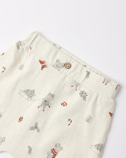 Close-up of a pair of cream-colored cotton shorts featuring a whimsical print of astronauts, Santa Claus, and holiday motifs, with a button closure at the waist.