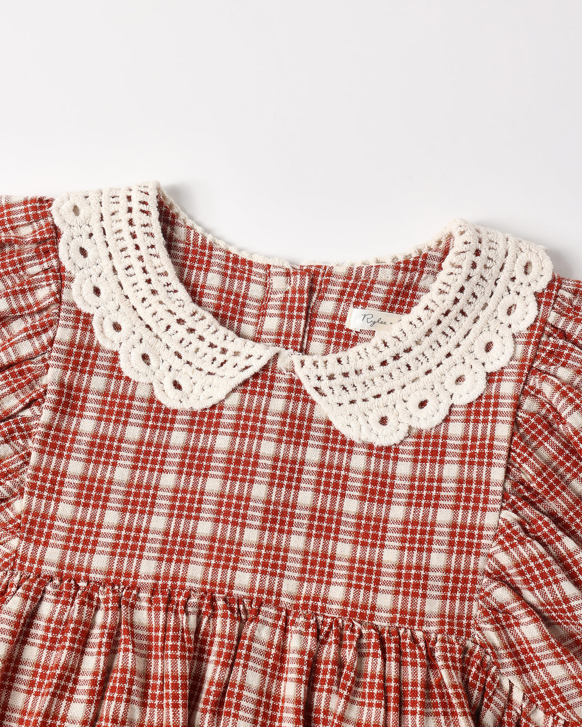 Close-up of a children's dress featuring a red and white gingham pattern with a prominent cream-colored crochet Peter Pan collar.