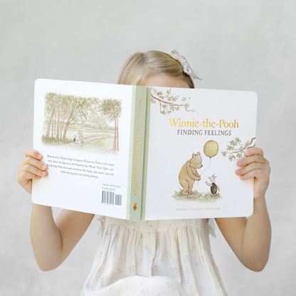 Girl holding the Winnie-the-Pooh: Finding Feelings board book open in front of her face