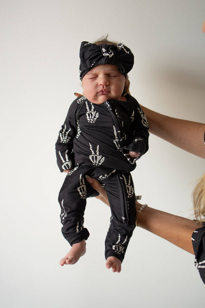 Baby held up wearing black Midnight Skelly bamboo zip pajamas and a matching beanie