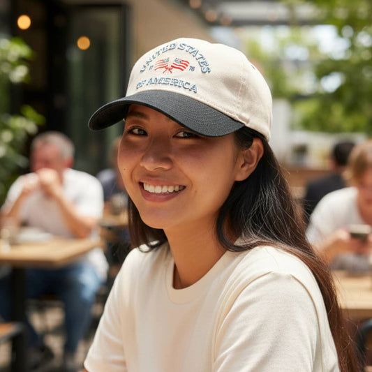 Woman wearing a cap with 'United States of America' text and an American flag, smiling outdoors.