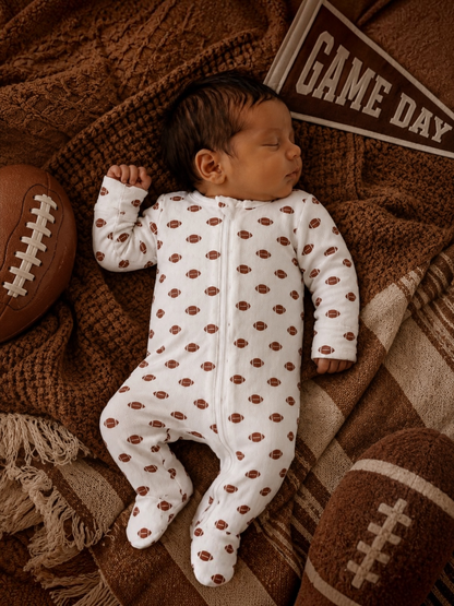 Baby lying on a football wearing the football print organic pointelle two-way zip footie