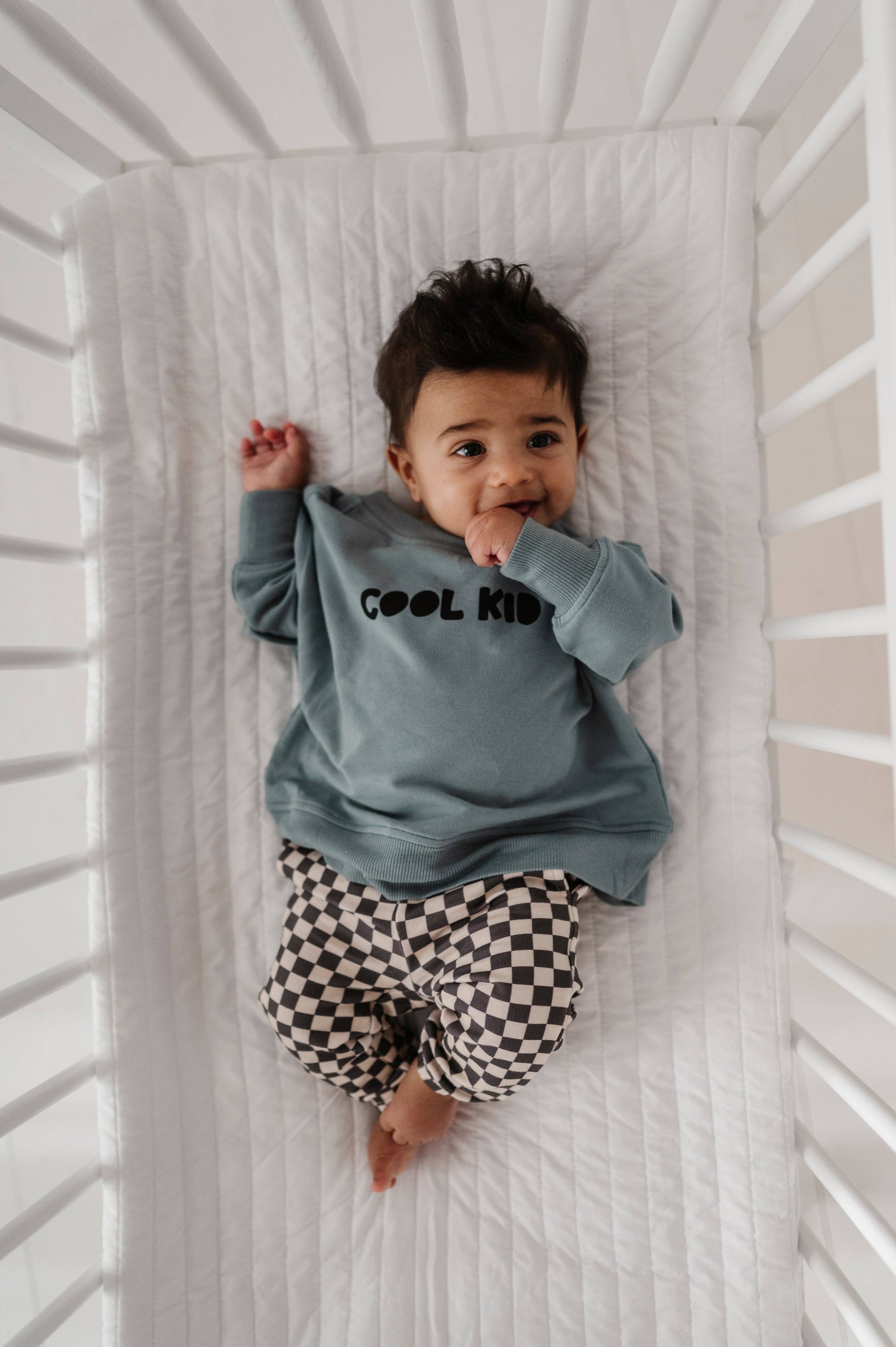 Boy laying down in crib wearing our checkered joggers and boxy cool kid sweatshirt. Our bamboo terry is made with 66% Bamboo 28% Cotton and 5% Spandex. 