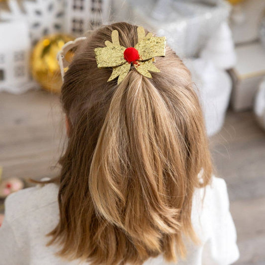 Back of girls head wearing gold glitter hair bow clip with red pom-pom accent and gold glitter antlers.