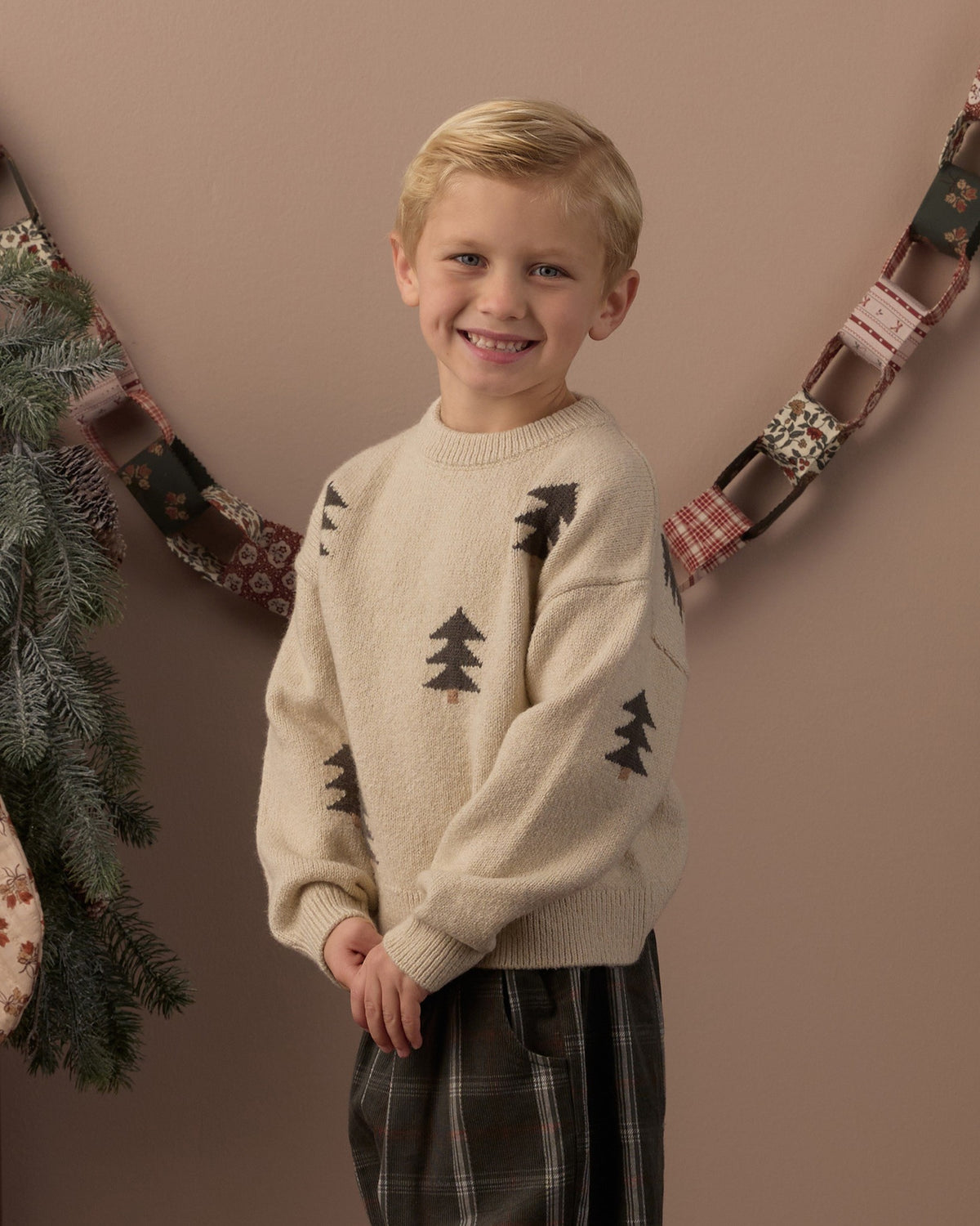 Boy smiling in the Rylee + Cru Aspen sweater with knit tree jacquard under a holiday garland