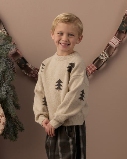 Boy smiling in the Rylee + Cru Aspen sweater with knit tree jacquard under a holiday garland