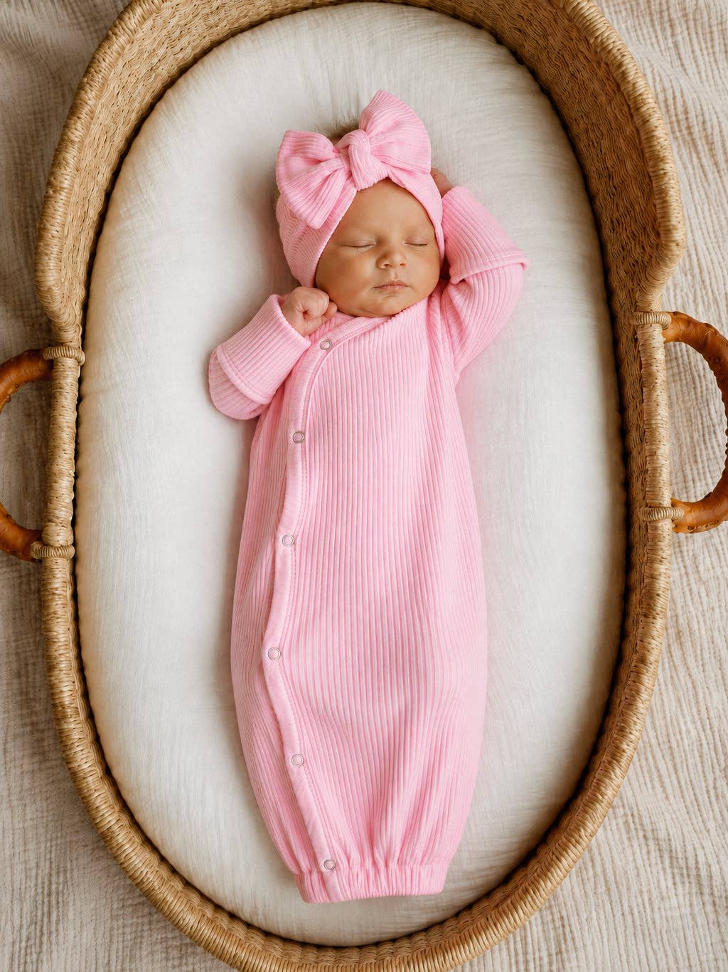 Baby in a pink ribbed knotted gown lying in a bassinet