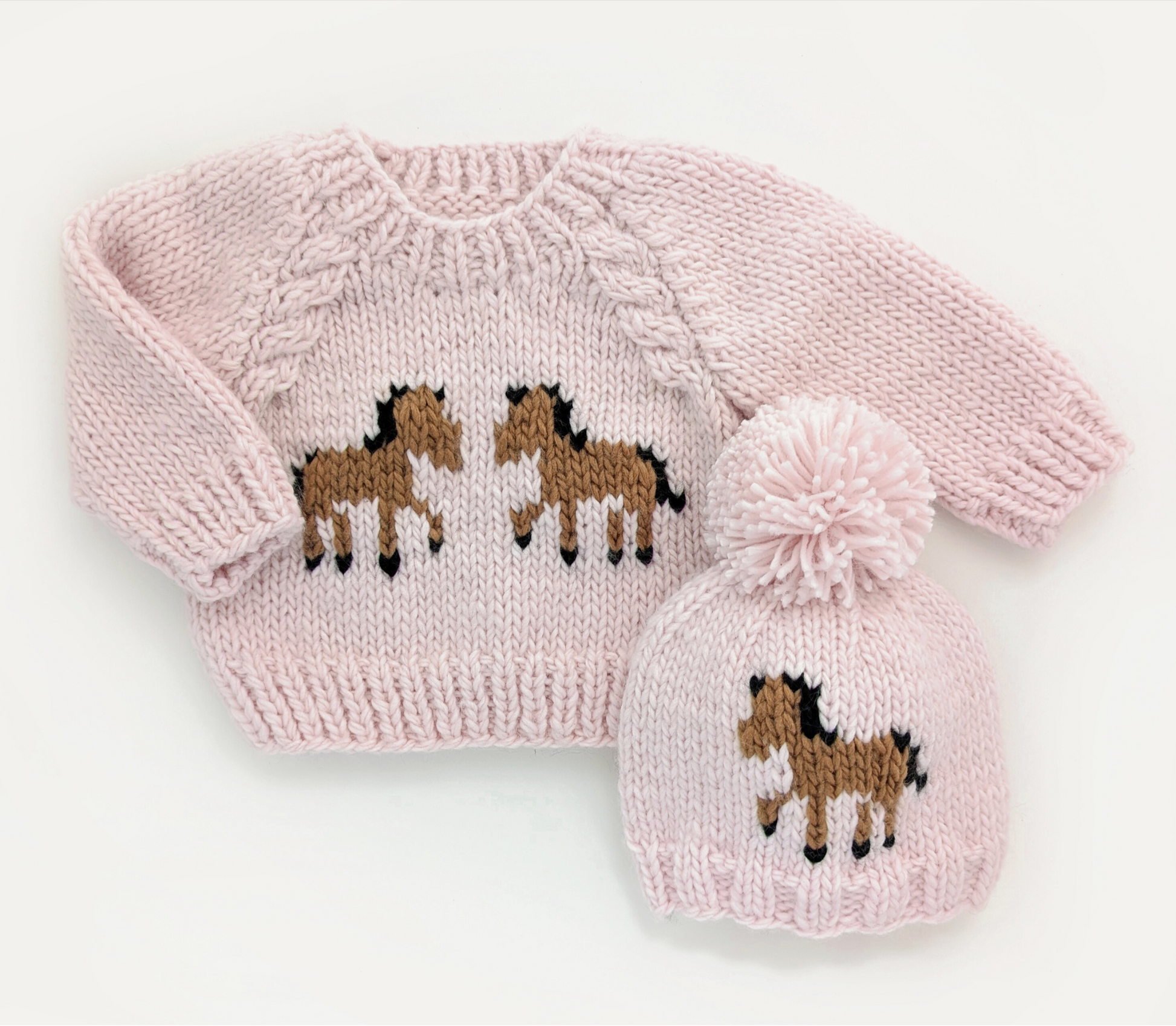 Pink knitted sweater and hat set with horse designs on a white background