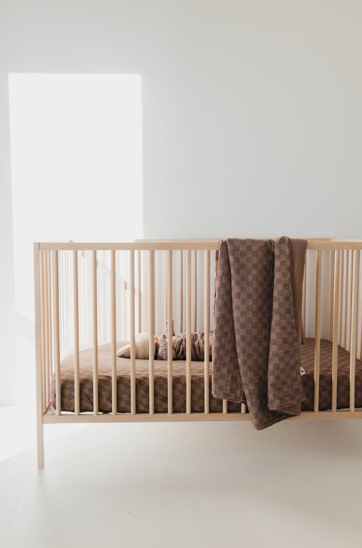 Brown checkerboard muslin quilt hanging over a crib rail in a neutral nursery