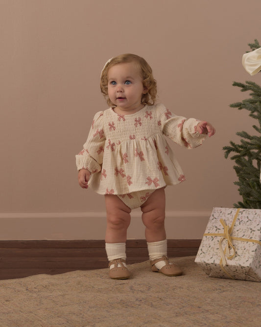 Toddler standing in the Rylee + Cru Sophia top and bloomer set in peppermint bows beside a small Christmas tree and wrapped gift