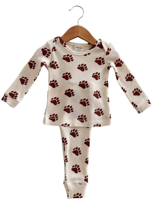 lay flat picture of bear paw two piece pajama set. The waffle pajamas are white with a brown bear paw pattern throughout. 