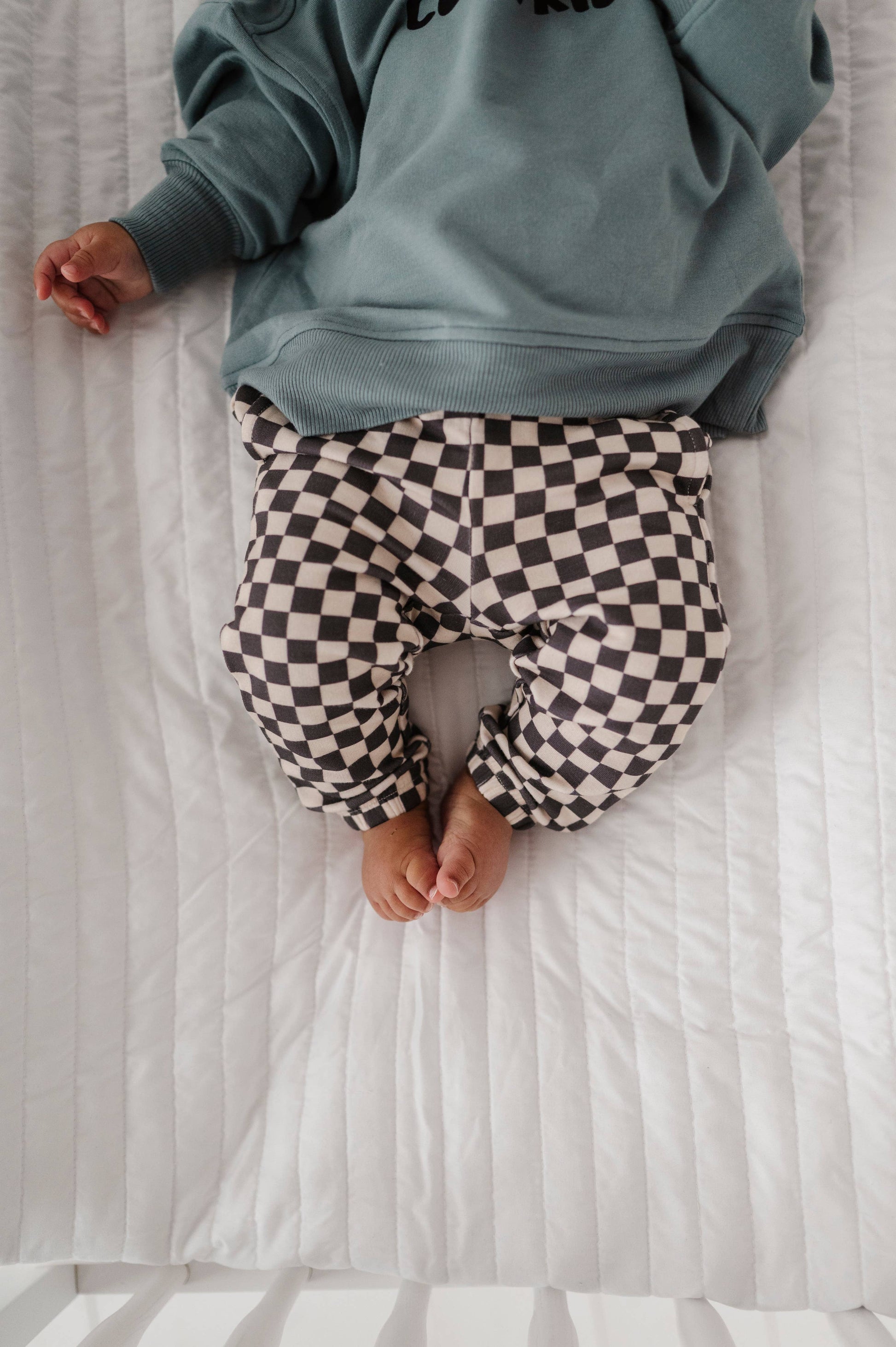 Boy laying down in crib wearing our checkered joggers and boxy cool kid sweatshirt. Our bamboo terry is made with 66% Bamboo 28% Cotton and 5% Spandex. 