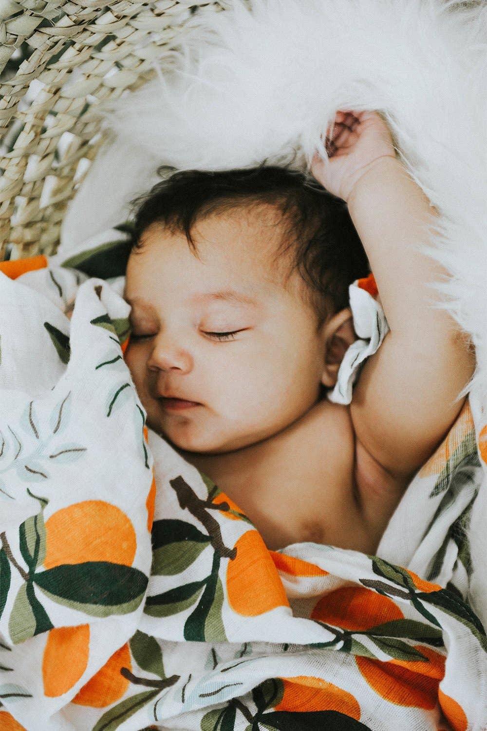 baby wrapped up in clementine swaddle. the mandarin oranges have green stems and leaves on them and are placed throughout either as a single clementine or in bunches of one or two clementines.