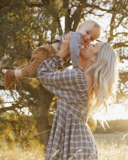 Mother holding a laughing baby in the Rylee + Cru Lucian pant in toffee under an oak tree at golden hour