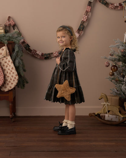 Girl in a dark plaid dress holding the Rylee + Cru gold star purse in a holiday-decorated room