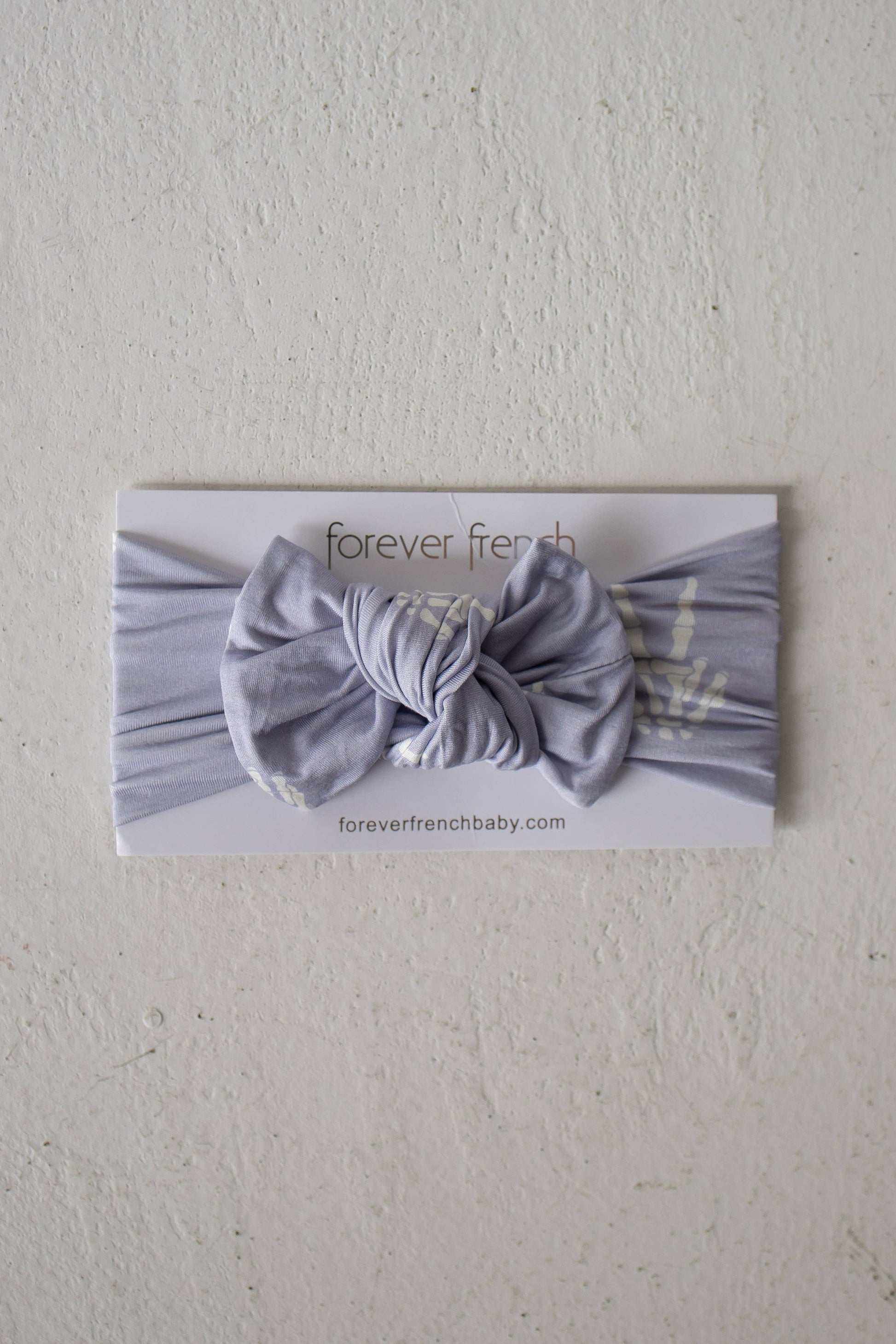 Forever French Baby Enchanted Skelly bamboo head wrap in lavender with a bow, shown on its packaging card